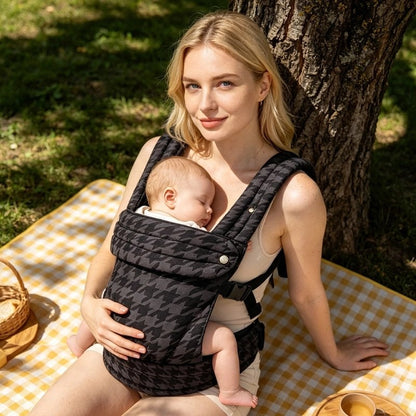 Porte bebe gris dans le quel dort bébé paisiblement porté par maman pendant pique-nique au parc